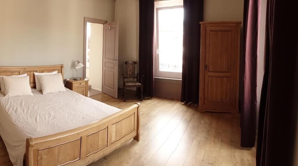 A bedroom with a wooden bed, a nightstand, a chair, a wardrobe, and a window with curtains.