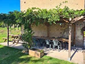 An outdoor patio with a wooden table and chairs, surrounded by a stone wall and greenery.