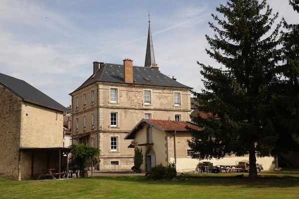 A two-story building with a prominent steeple, a covered outdoor seating area, and a well-maintained lawn.