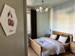 A bedroom with a wooden bed, a nightstand, a lamp, and a window with curtains.