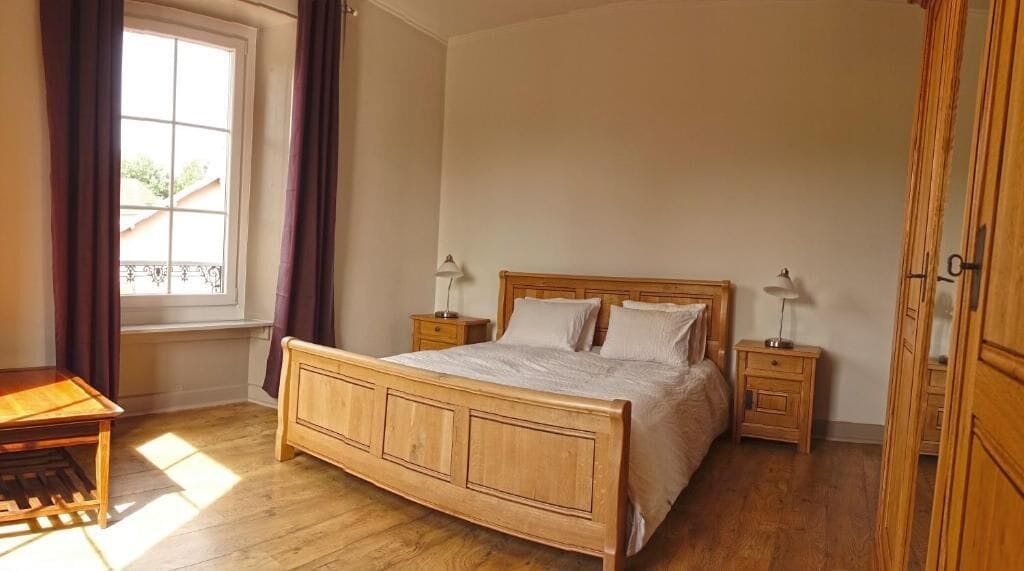Ein Schlafzimmer mit einem hölzernen Bett, zwei Nachttischen, einem fensterbelaubten Fenster und einem Holzboden.