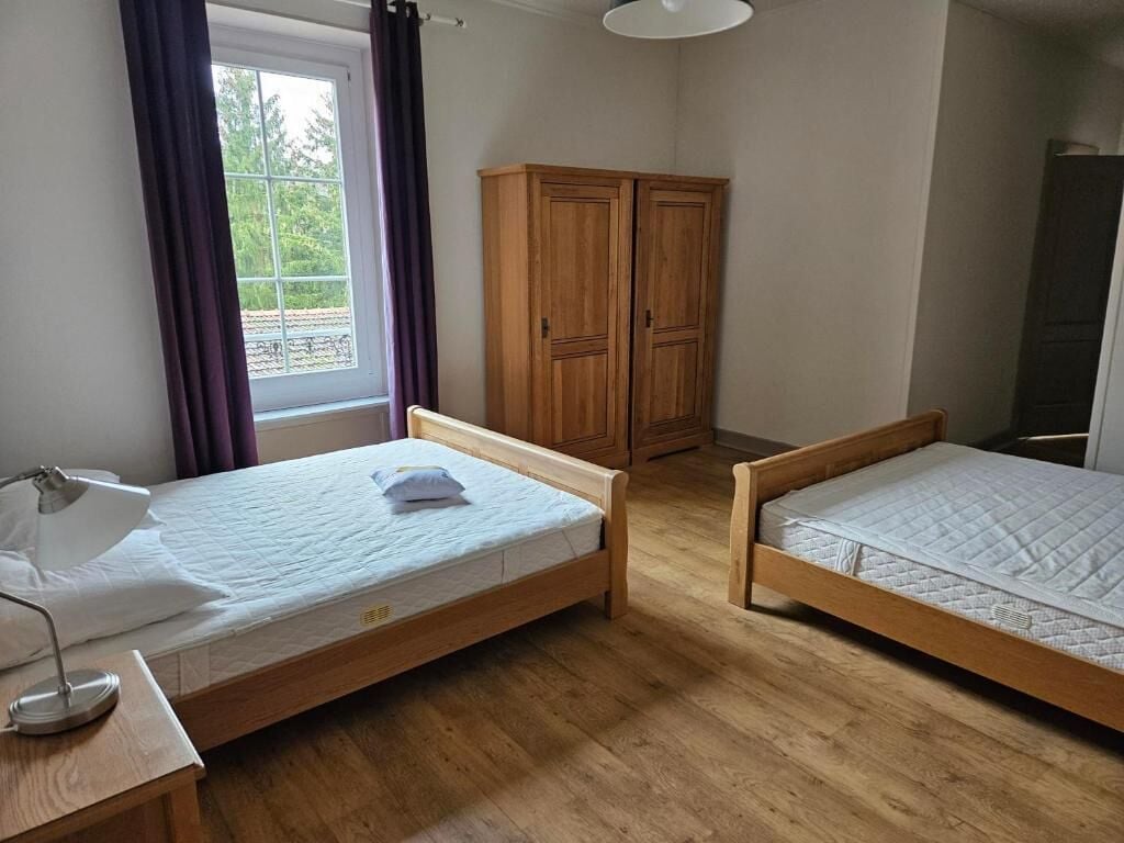 A room with two wooden beds, a desk with a lamp, a window with curtains, and a wardrobe.