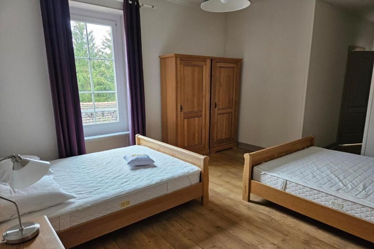 A room with two wooden beds, a desk with a lamp, a window with curtains, and a wardrobe.