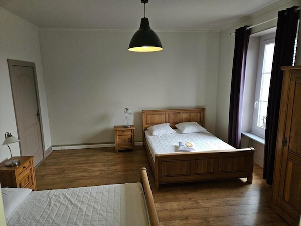 A bedroom with a wooden bed, a bedside table, a nightstand, a hanging light fixture, and a window with curtains.