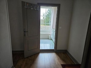 A room with a wooden floor, a door leading to a balcony, and a window with a view of the outside.