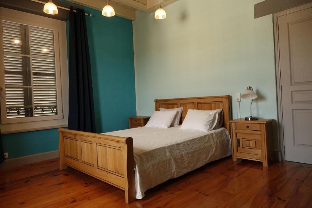 Een slaapkamer met een houten bed, een nachtkastje, een raam met jaloezieën en een deur.