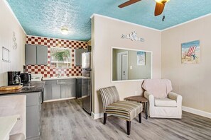 A compact kitchen with checkered backsplash, a dining area with striped chairs, and a ceiling fan. - Cozy coastal escape near the beach & shopping with fast WiFi, AC (Tybee Island)