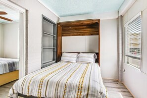 Ein Schlafzimmer mit einem Bett, einem hölzernen Kopfende, einem Fenster mit Jalousien und einer Tür.