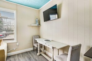 Ein Zimmer mit einem weißen Tisch, einem grauen Stuhl, einem an der Wand befestigten Fernseher und einem Fenster mit Jalousien.