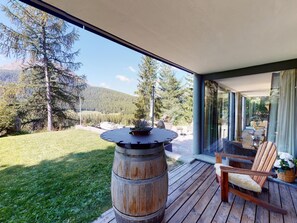 Eine Holzterrasse mit einem Fassentisch, einem Stuhl und Blick auf eine bewaldete Berglandschaft.