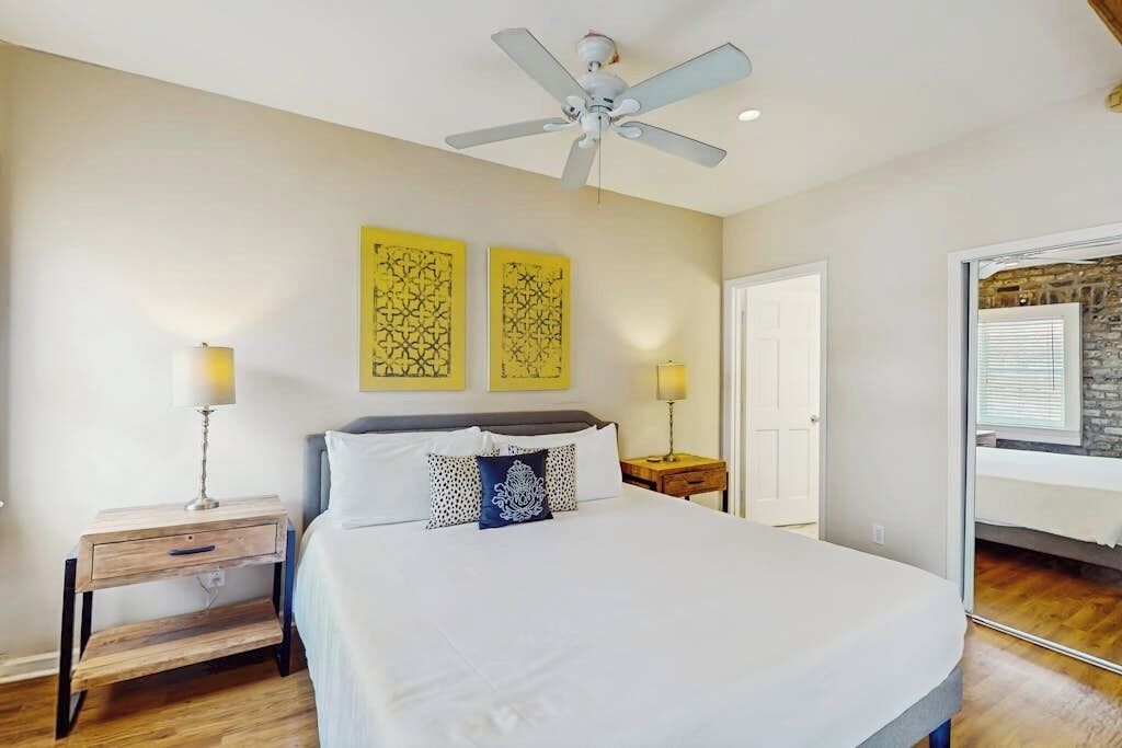 A bedroom with a bed, two bedside tables, a ceiling fan, and two wall-mounted lamps.