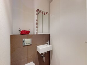 Une salle de bain avec un lavabo blanc, un miroir et un panier rouge accroché au mur.