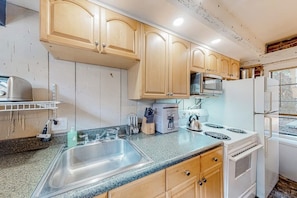 A kitchen with wooden cabinets, a stainless steel sink, a stove, and a microwave. - Atmospheric carriage house steps from Forsyth Park, great for long stays (Savannah)