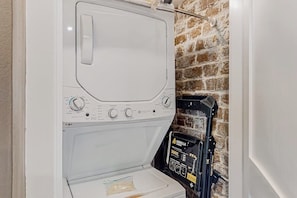 A compact, white washing machine with a control panel, located in a room with a brick wall. - Atmospheric carriage house steps from Forsyth Park, great for long stays (Savannah)