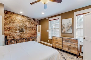 A bedroom with a brick wall, a bed, a dresser, and a ceiling fan. - Atmospheric carriage house steps from Forsyth Park, great for long stays (Savannah)