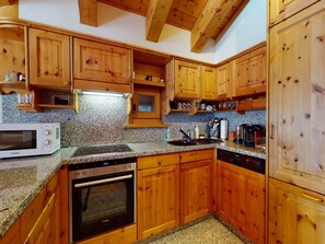 A kitchen with wooden cabinets, granite countertops, a microwave, a stove, and a dishwasher. - Apartment Polaschin B12 by Interhome (Sils Maria)