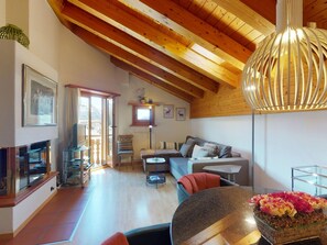 A spacious living room with a high ceiling, wooden beams, a sofa set, a dining table, and a large window. - Apartment Polaschin B12 by Interhome (Sils Maria)
