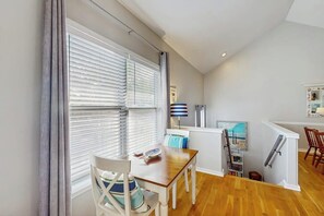A dining area with a wooden table and chairs, a window with blinds, a lamp, and a painting on the wall. - Seaside serenity home with beach access, washer/dryer, & dog-friendly (Tybee Island)