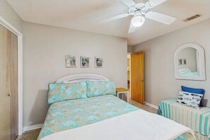 A bedroom with a bed, a ceiling fan, a small table with a chair, and a mirror on the wall. - Seaside serenity home with beach access, washer/dryer, & dog-friendly (Tybee Island)
