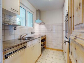 Una cocina compacta con armarios blancos, un lavamanos de acero inoxidable y un horno empotrado.