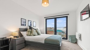 A bedroom with a bed, bedside tables, a lamp, a TV, and a view of the outside. - Central Liverpool 2 Bedroom Apartment, Large, Modern, WIFI, Sleeps 4 (Liverpool)