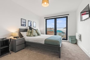 Ein Schlafzimmer mit Bett, Nachttischen, einer Lampe, einem Fernseher und Blick ins Freie.