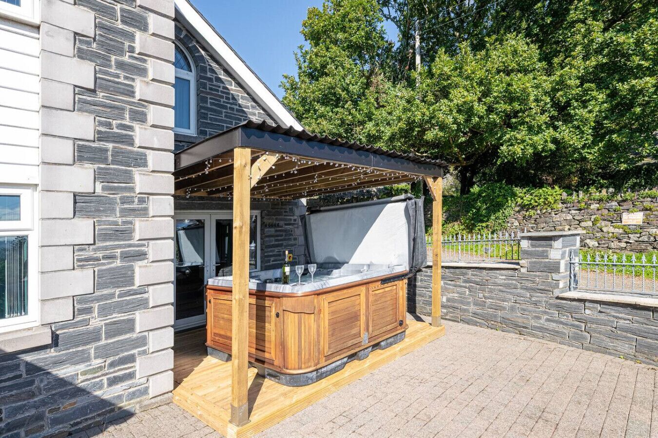 A hot tub under a pergola with stone walls and a wooden deck.