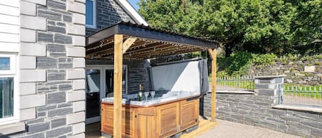 A hot tub under a pergola with stone walls and a wooden deck.