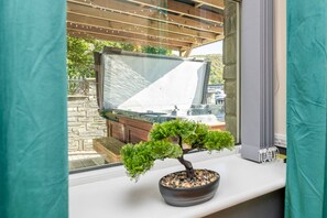A window with a view of a stone patio and a wooden pergola. - Hot Tub 3BR Flat Near Snowdon | Parking | Sleeps 6 (Penmorfa)