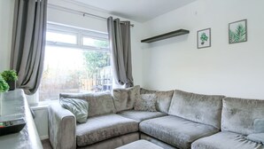 A living room with a grey sectional sofa, a small table with a plant, and a window with curtains. - Modern 2BR Apartment, S1 City Centre, WIFI, Sleeps 6 (Greater Manchester)