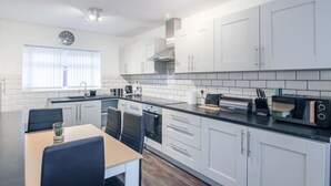 A modern kitchen with white cabinets, a black countertop, and a dining area with a table and chairs. - Modern 2BR Apartment, S1 City Centre, WIFI, Sleeps 6 (Greater Manchester)