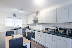A modern kitchen with white cabinets, a black countertop, and a dining area with a table and chairs. - Modern 2BR Apartment, S1 City Centre, WIFI, Sleeps 6 (Greater Manchester)