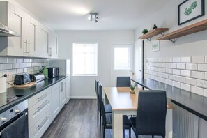 Une cuisine moderne avec des meubles blancs, un plan de travail noir et un coin repas comprenant une table et des chaises.