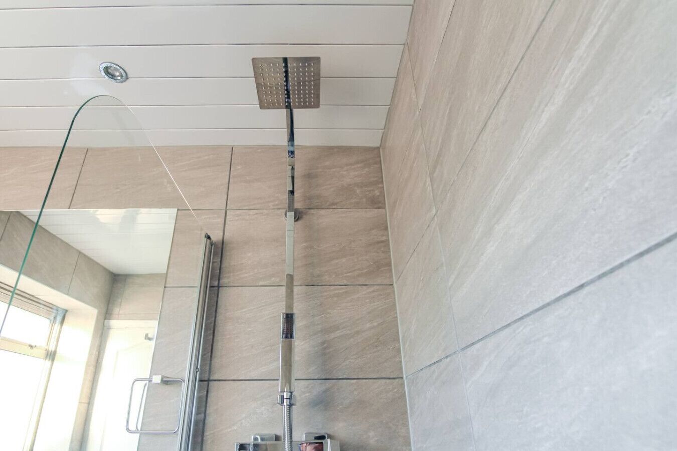 A modern bathroom with a glass shower enclosure, a visible showerhead, and a tiled floor.