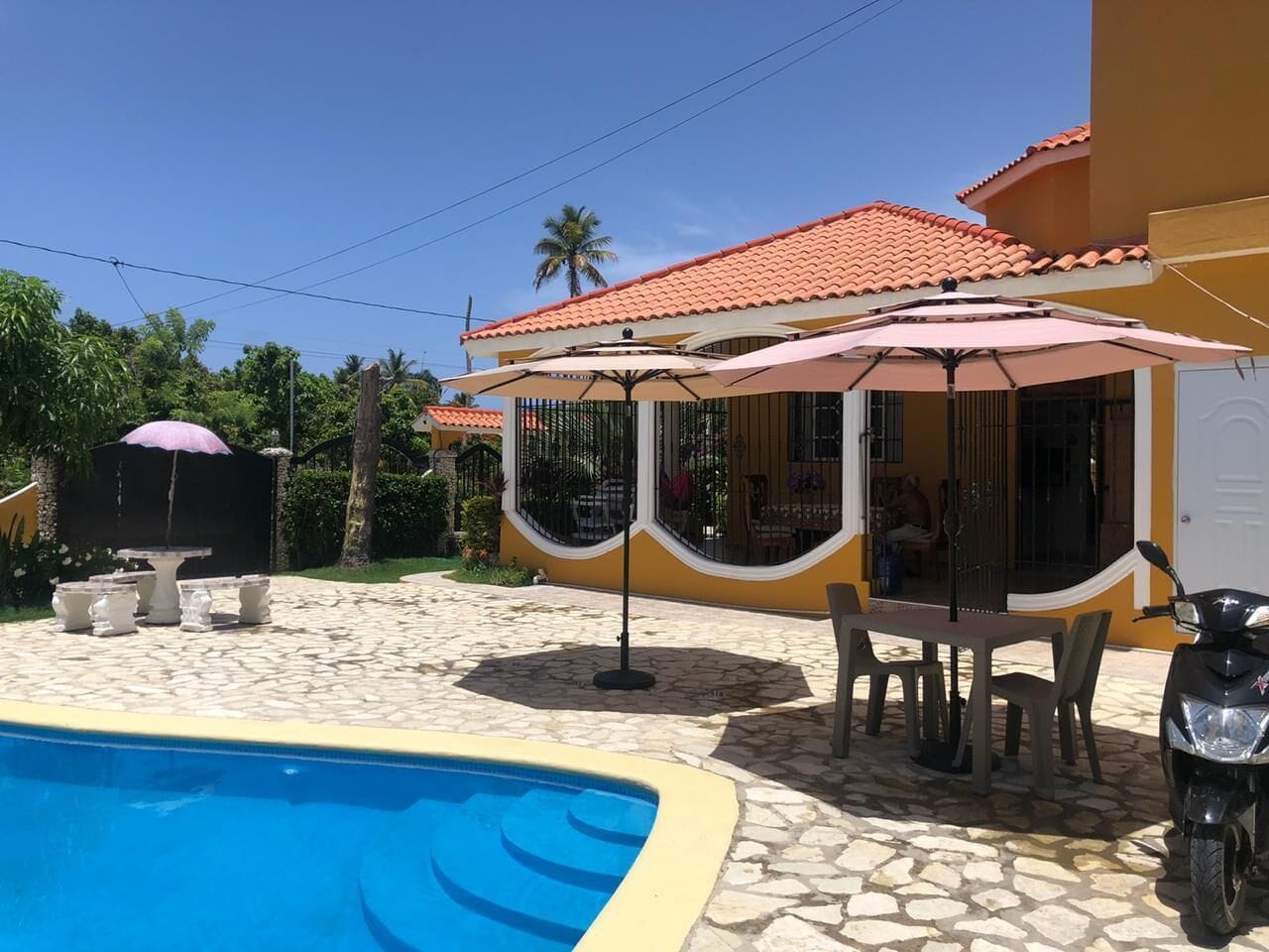 A pool area with a tiled deck, outdoor furniture, and umbrellas.