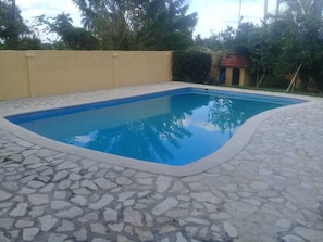 A swimming pool with a stone-tiled deck, surrounded by a low wall and vegetation.