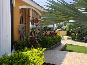 Una propiedad residencial con acceso mediante portón, un camino pavimentado y diversas plantas.