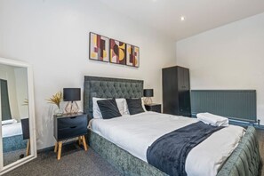 Ein modernes Schlafzimmer mit einem großen Bett, Nachttischen, einem Kleiderschrank und abstrakter Wandkunst.