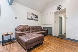 Ein Zimmer mit braunem Ledersofa, einem kleinen Holfnachtkästchen und einer an der Wand befestigten Uhr.