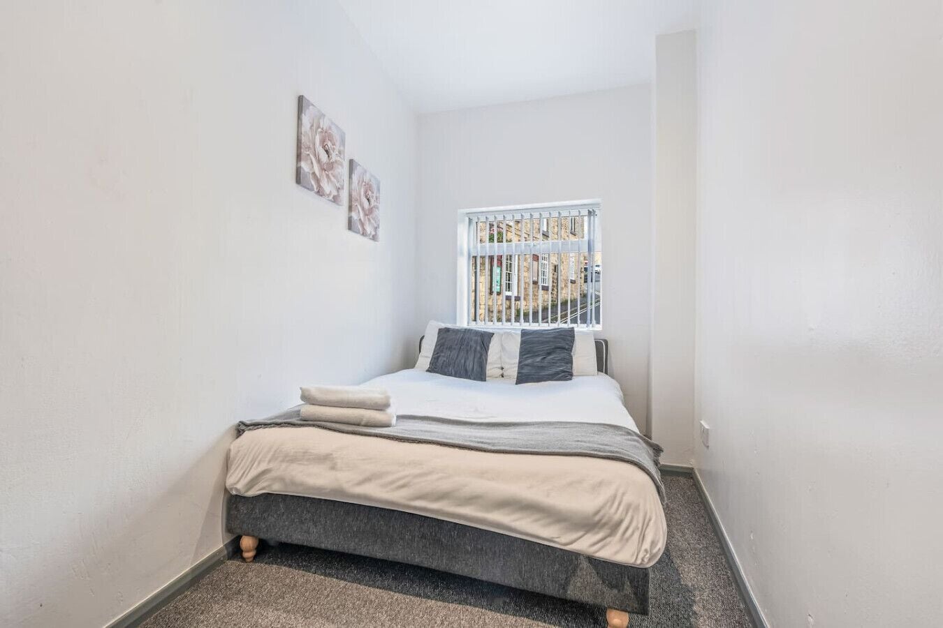 A small bedroom with a single bed, a window with a view of buildings, and two wall-mounted artworks.