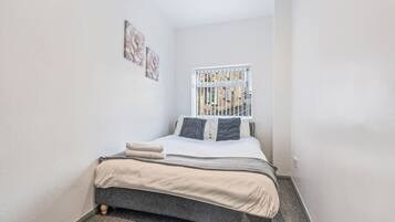 A small bedroom with a single bed, a window with a view of buildings, and two wall-mounted artworks.