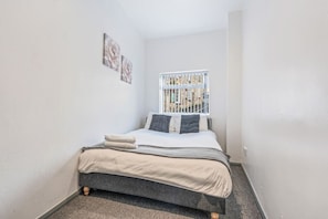 A small bedroom with a single bed, a window with a view of buildings, and two wall-mounted artworks. - Stylish Homely Flat|Parking|4 Beds|6 Guests (Sheffield)
