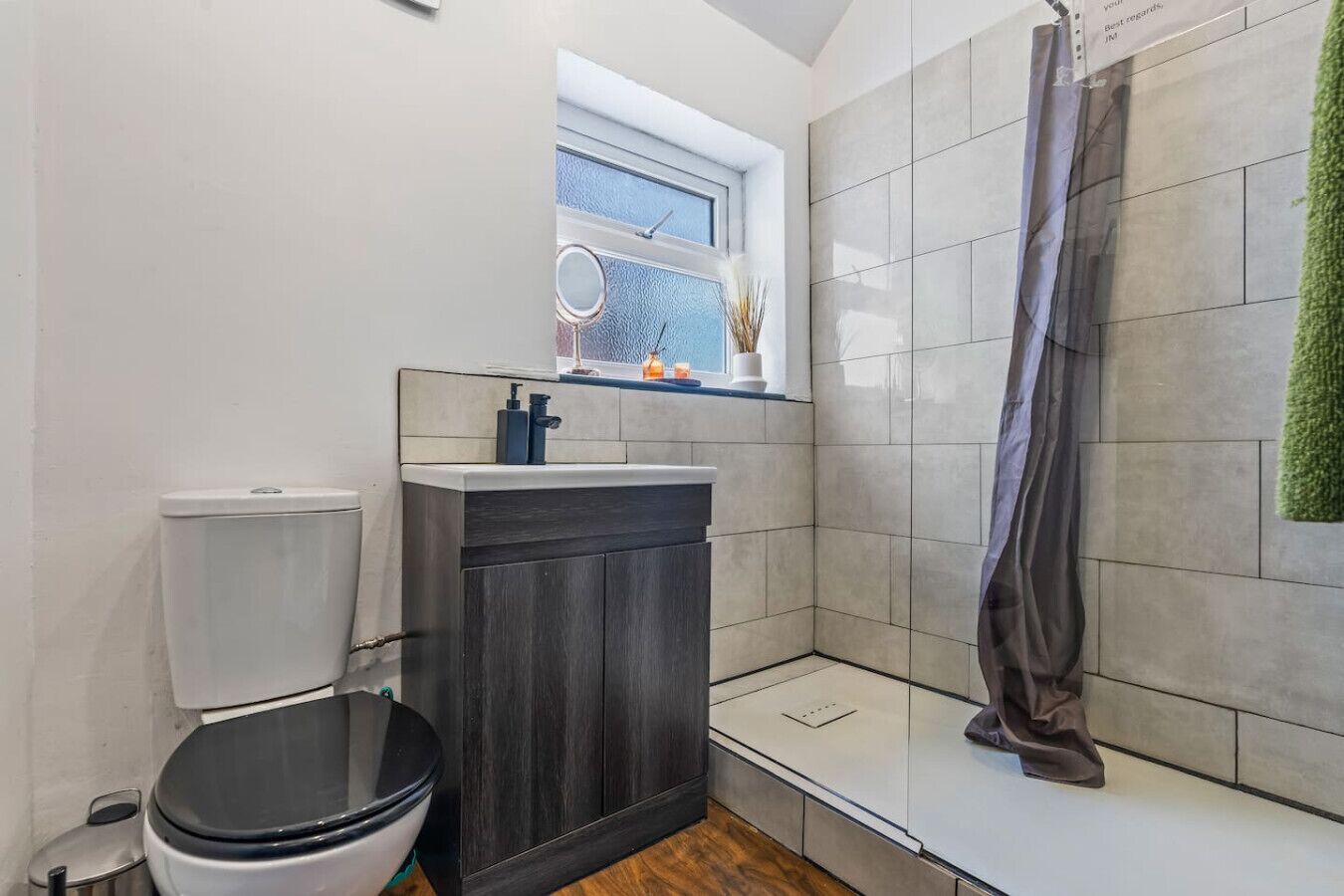 A modern bathroom with a toilet, dark wooden cabinet, and a shower area.