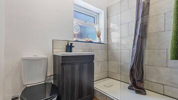 A modern bathroom with a toilet, dark wooden cabinet, and a shower area.
