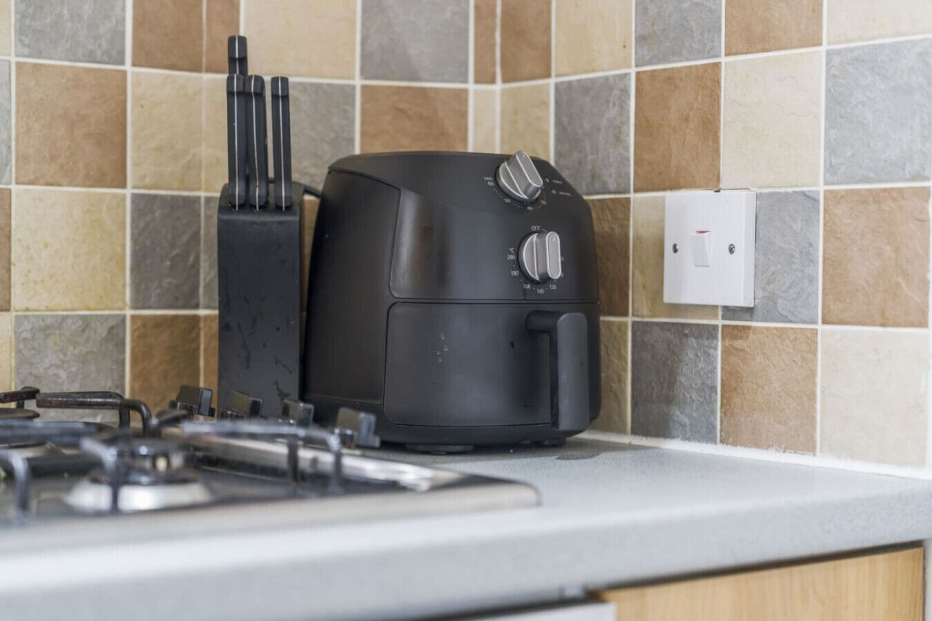 Eine Küche mit einem schwarzen Toaster auf einer Arbeitsplatte, einem Gasherd und einer gefliesten Spritzwand.