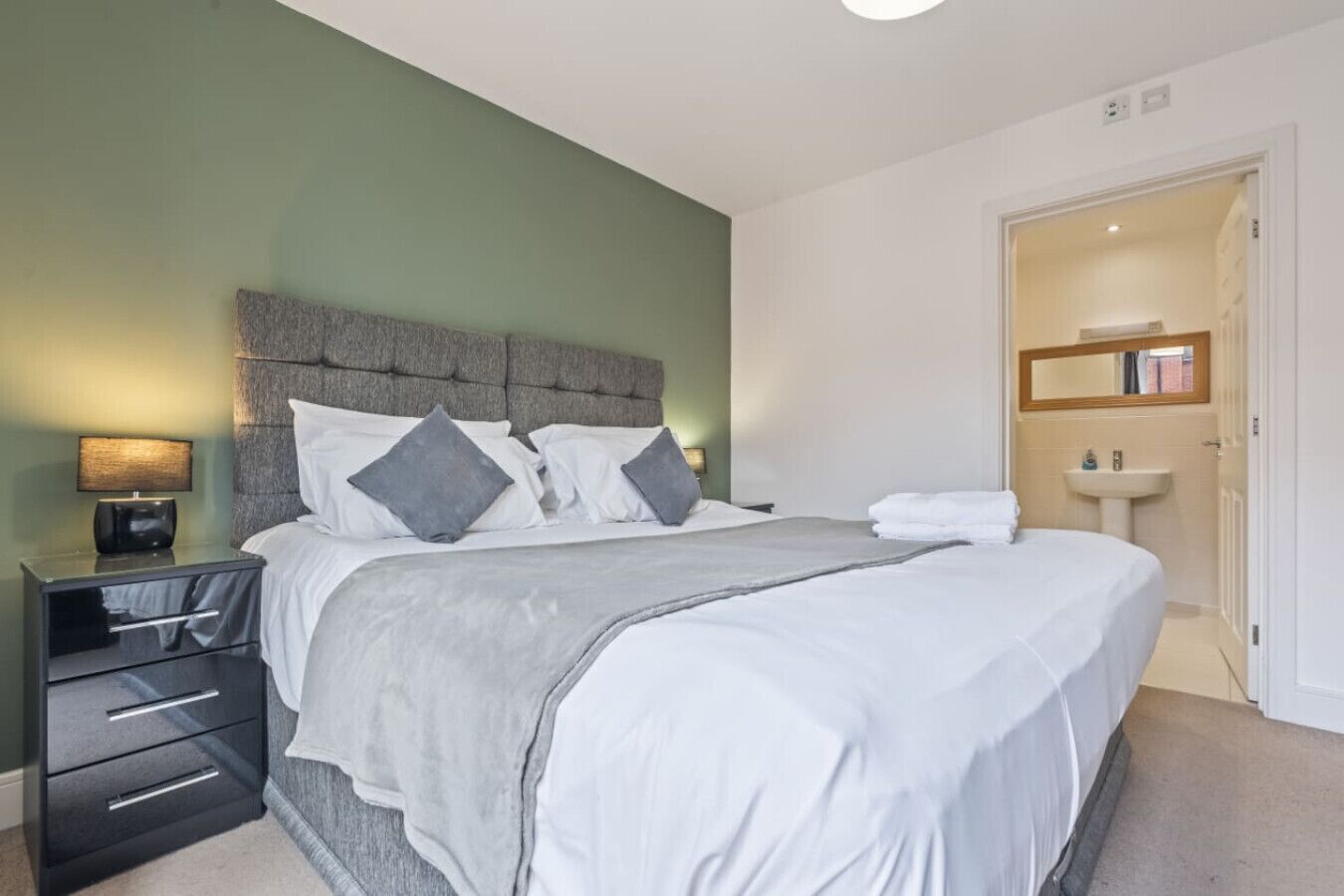 A hotel room with a bed, bedside tables, a lamp, a mirror, and a door leading to a bathroom.