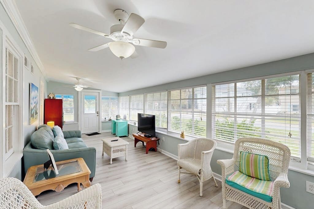 A spacious living room with a ceiling fan, a sofa, a coffee table, a television, and wicker chairs.