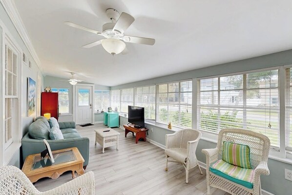A spacious living room with a ceiling fan, a sofa, a coffee table, a television, and wicker chairs. - Beachy dog-friendly home, blocks to the restaurants, fishing pier & beach (Tybee Island)