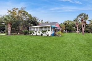 A house with a large glass windowed porch, surrounded by a well-maintained lawn and palm trees. - Beachy dog-friendly home, blocks to the restaurants, fishing pier & beach (Tybee Island)