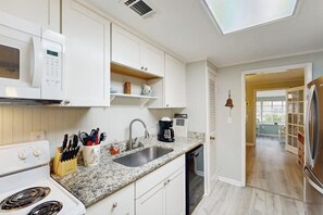 A kitchen with white cabinets, a granite countertop, a built-in microwave, a coffee maker, and a dishwasher. - Beachy dog-friendly home, blocks to the restaurants, fishing pier & beach (Tybee Island)